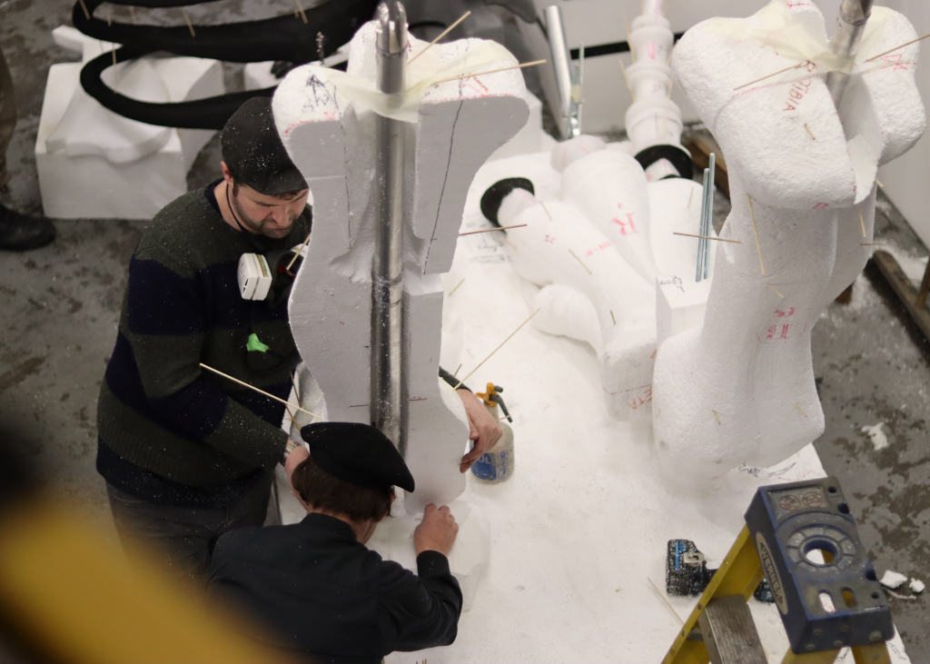 Sculptures are seen putting together the large dinosaur's foam legs.